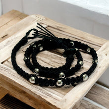 Load image into Gallery viewer, A black hemp necklace with metal beads displayed on a wooden surface.