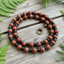 Load image into Gallery viewer, A handcrafted necklace with a combination of red and black jasper gemstone beads, antiqued brass beads, and coconut shell beads, finished with a brass lobster clasp.