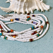Load image into Gallery viewer, A multi-strand beaded necklace made of small white disc beads with scattered colorful spacer beads in blue, orange, red, purple, and green, arranged on a light blue textured surface with a white seashell behind it.