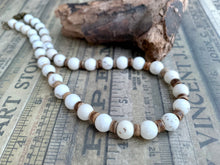Load image into Gallery viewer, A beaded necklace made of white round beads separated by small brown wooden spacers, displayed on vintage newspaper print with a piece of driftwood behind it.