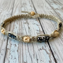 Load image into Gallery viewer, A thick hemp necklace with carved skull bone beads displayed on a flat surface.