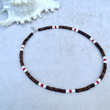 Load image into Gallery viewer, A choker necklace with brown litub puka shell beads, red and white waxed coconut heishi beads, and clear glass beads, displayed against a neutral background with a shell to the side.