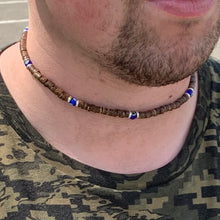 Load image into Gallery viewer, A person wearing a choker necklace made of waxed coconut beads and blue glass beads, with a patterned shirt in the background.