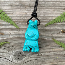 Load image into Gallery viewer, A bear totem necklace with a turquoise magnesite pendant resting on a piece of paper with a sliding knot adjusting system, displayed alongside a natural object for scale.