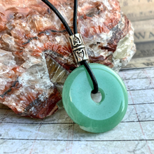 Load image into Gallery viewer, A green aventurine donut pendant on a black leather cord choker necklace, displayed on a wooden surface.
