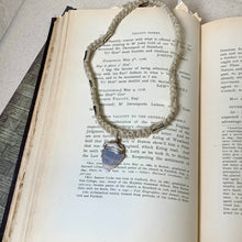 Load image into Gallery viewer, A vintage pair of metal tweezers with a blue and silver striped patterned handle, resting on the pages of an open antique book.
