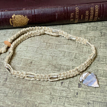 Load image into Gallery viewer, A handmade macrame-style beaded bracelet with a faceted iridescent moonstone pendant, displayed on a textured gray surface with a vintage book in the background.
