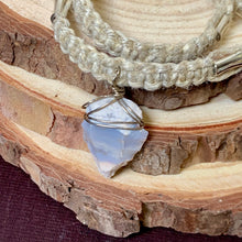 Load image into Gallery viewer, A close-up of a handmade double-strand braided cord bracelet with a raw, irregular-shaped pale blue stone pendant wrapped in silver wire, displayed on a rustic wood slice.
