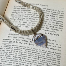 Load image into Gallery viewer, A silver-toned metal key with a decorative floral engraving rests on an open vintage book page featuring printed text and a gold pen.
