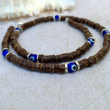 Load image into Gallery viewer, A handcrafted tribal necklace made with natural coconut beads and blue Evil Eye glass beads, featuring metallic beads and a waxed cord.
